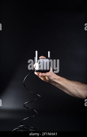 Hand hält schwarzen WiFi-Router auf schwarzem Hintergrund mit angeschlossenem Kabel. Stockfoto