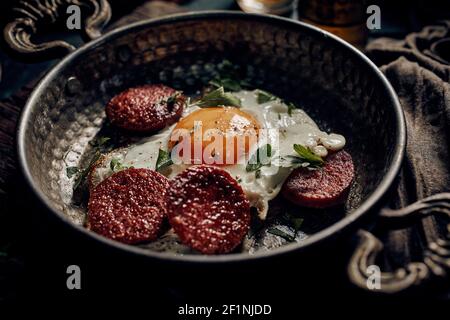 Hoher Winkel von appetitlichen Sucuklu Yumurta traditionelle Gericht aus Spiegeleier und Würstchen in der Pfanne auf dem Tisch serviert Traditionelles türkisches Frühstück Stockfoto