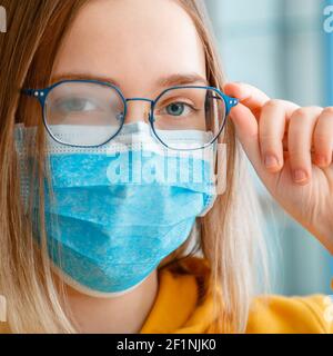 Neblige Brille trägt auf junge Frau. Nahaufnahme Porträt. Teenager Mädchen in blau medizinische Schutzmaske und Brillen Tücher verschwommen neblig beschmiert Stockfoto