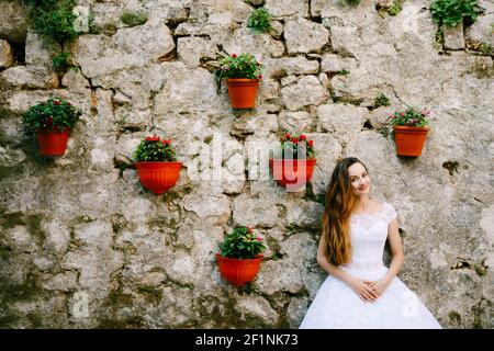 Die Braut im zarten Brautkleid steht in der Nähe Wand von Altes Gebäude mit Blumentöpfen in Perast dekoriert Stockfoto