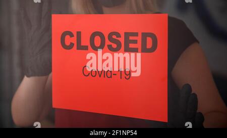 Rotes Warnschild geschlossen covid 19 Lockdown am Vordereingang Tür als neue normale Abschaltung im Restaurant.Frau in schützenden medizinischen Maske Handschuhe hängen Klo Stockfoto