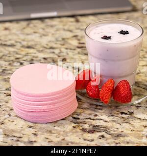 Ein köstlicher Erdbeer- und Brombeersmoothie mit einem Erdbeer-Wafer-Snack, der eine Pause von der Arbeit am Computer macht. Stockfoto
