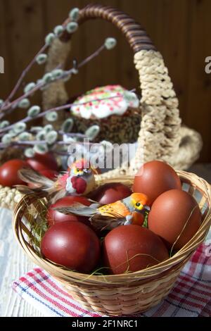 Spielzeugvögel sitzen in einem Weidenkorb auf bemalten Eiern. Im Mittelpunkt der Kuchen- und Weidenzweige. Stockfoto