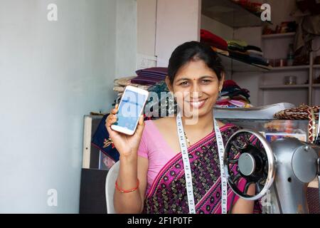 Indische Textilarbeiterin zeigt Mobiltelefon in der Werkstatt Stockfoto