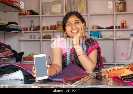 Indische Textilarbeiterin zeigt Mobiltelefon in der Werkstatt Stockfoto