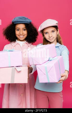 Interracial Kinder in stilvollen Frühling Kleidung posiert mit Geschenkboxen Isoliert auf rosa Stockfoto