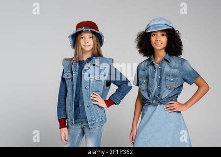 Modische interracial Kinder in Denim Kleidung und Hüte posiert mit Hände auf Hüften auf grau Stockfoto
