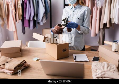 Beschnittene Ansicht des Verkäufers in medizinischer Maske und Latexhandschuhen, die Schuh im Ausstellungsraum halten, verschwommener Vordergrund Stockfoto