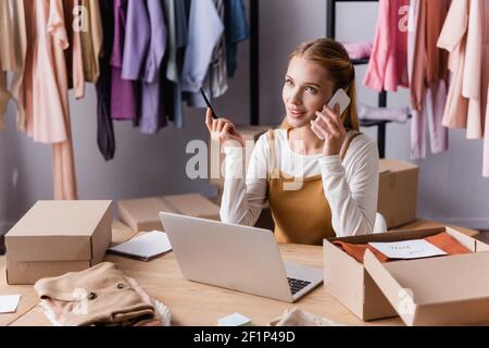 Positive Showroom Inhaber Annahme der Bestellung auf dem Smartphone in der Nähe von Laptop und Pakete Stockfoto