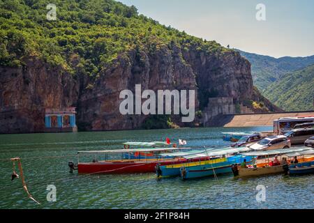 Koman-See, Albanien – 8. August 2020: Sommerlandschaft - albanische Berge, bedeckt mit üppigem Laub, See mit ruhigem blauem Wasser und bunte Kreuzfahrt Stockfoto