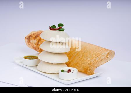 Ghee Roast Dosa und Idlii, südindisches Hauptfrühstück, das wunderschön auf einem weißen Teller mit Bananenblatt und Curry als Samba angeordnet ist Stockfoto