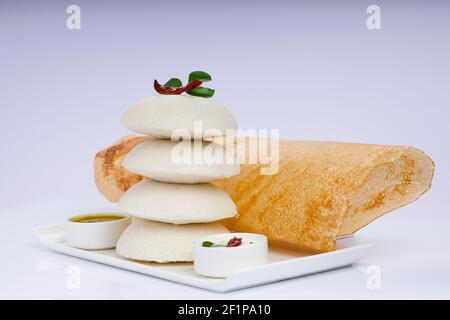 Ghee Roast Dosa und Idlii, südindisches Hauptfrühstück, das wunderschön auf einem weißen Teller mit Bananenblatt und Curry als Samba angeordnet ist Stockfoto