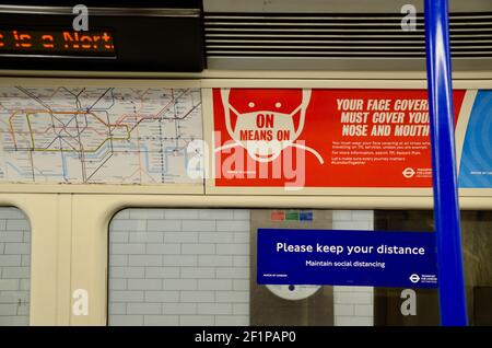 Passagiere und covid 19 Pandemie Gesicht Abdeckung und soziale Distanzierung Schilder auf die londoner U-Bahn-Züge 2021 Stockfoto