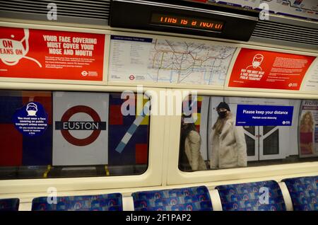 Passagiere und covid 19 Pandemie Gesicht Abdeckung und soziale Distanzierung Schilder auf die londoner U-Bahn-Züge 2021 Stockfoto