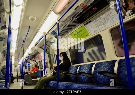 Passagiere und covid 19 Pandemie Gesicht Abdeckung und soziale Distanzierung Schilder auf die londoner U-Bahn-Züge 2021 Stockfoto