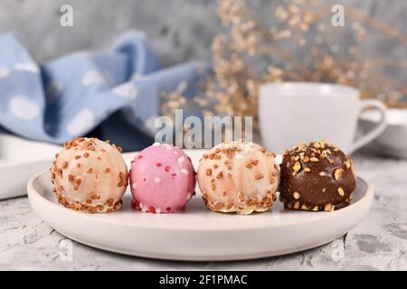 Kleine bunte Kuchenkugeln glasiert mit weißer, rosa und brauner Schokolade mit Streuseln in einer Reihe auf weißem Teller Stockfoto