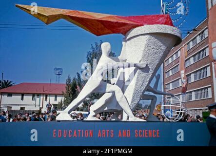 Paradewagen zur Förderung von Bildung, Kunst und Wissenschaft, während der Apartheid-Ära, Durban, Südafrika, 1966. Der Schwimmer zeigt eine moderne ‘Skulptur’ einer Figur, die eine Fackel mit Flammen hält, die aus ihr aufsteigen. Es ist sehr viel ein weißes Publikum Betrachten dieses Ereignis. Dieses Bild ist von einem alten Amateur 35mm Kodak Farbtransparenz. Stockfoto