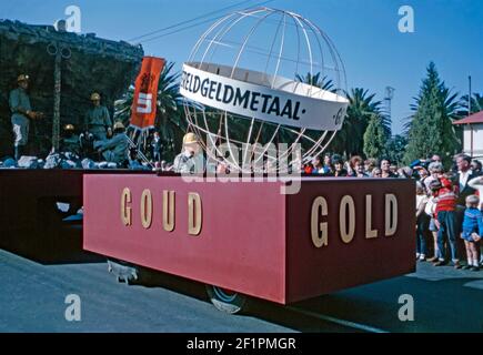 Parade-Festwagen zur Förderung des südafrikanischen Goldbergbaus (Goud in Afrikaans), während der Apartheid-Ära, Durban, Südafrika, 1966. Der Traktor zieht einen Anhänger mit Goldgräbern auf ihm ‘bohren’ für das Edelmetall. Es ist sehr viel ein weißes Publikum Betrachten dieses Ereignis. Dieses Bild ist von einem alten Amateur 35mm Kodak Farbtransparenz. Stockfoto