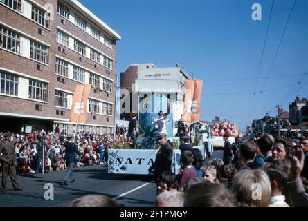 Parade-Festwagen zur Förderung der Provinz Natal, während der Apartheid-Ära, Durban, Südafrika, 1966. Der Festwagen wurde mit Fauna und Flora aus der Gegend geschmückt. Es ist sehr viel ein weißes Publikum Betrachten dieses Ereignis. Die Provinz Natal war von 1910 bis 1994 eine Provinz Südafrikas. Ländliche Gebiete, die von der schwarzafrikanischen Bevölkerung Natal (dem Bantustan von KwaZulu) bewohnt wurden, wurden 1981 teilweise autonom. Die erste nicht-rassische Wahl war 1994. In diesem Jahr wurde der KwaZulu-Bantustan in Natal reinkorporiert und die Provinz in KwaZulu-Natal umbenannte – ein Vintage-Foto aus dem Jahr 1960s. Stockfoto