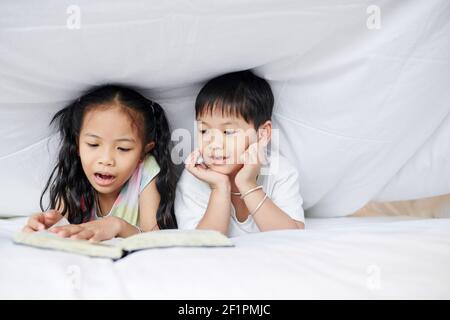 Kleiner vietnamesischer Bruder und Schwester liegen unter der Decke und lesen Ein Buch Stockfoto