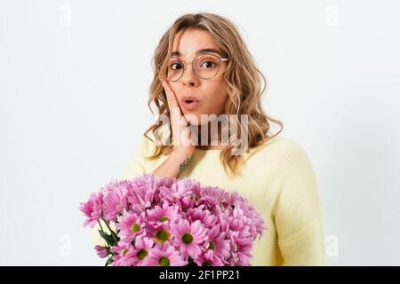 Porträt der überrascht junge Frau mit Blumenstrauß auf weißem Studio Hintergrund stehend Blick in die Kamera mit angenehm schockiert Ausdruck. Stockfoto