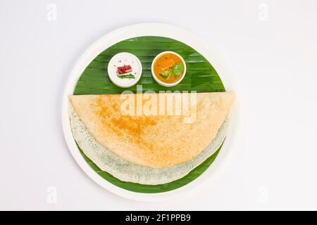 Ghee Roasted Dosa, südindisches Hauptfrühstück, das wunderschön wie ein lächelndes Gesicht auf einem weißen Teller mit Bananenblatt angeordnet ist. Stockfoto