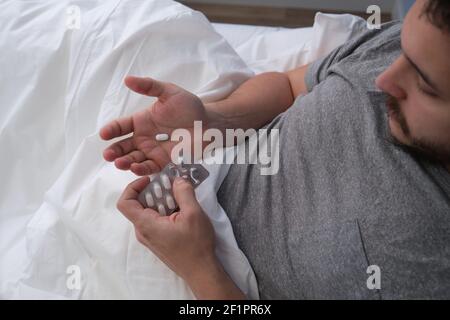 Junger latein erkrankt im Bett und nimmt eine Pille. Gefühl krank Konzept. Stockfoto