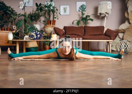 Junge sportliche Frau praktiziert Yoga zu Hause tun Stretching Übung die Mitte Split Pose, gerade Winkel Pose. Samakonasana. Spreitel aufsetzen Stockfoto