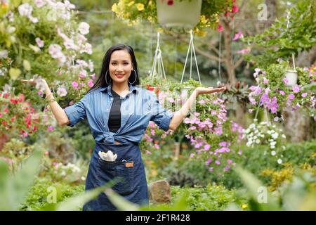 Ziemlich attraktive junge asiatische Frau in Denim kurz und Schürze Begrüßung der Kunden in ihrer Blumenkühe Stockfoto