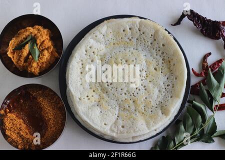Indische Pfannkuchen werden auch als Dosa mit einem fermentierten Teig aus Reis und Linsen gemacht bekannt. Serviert mit idli podi chutney, sambar, Coconut Chutney und einem Glas Stockfoto