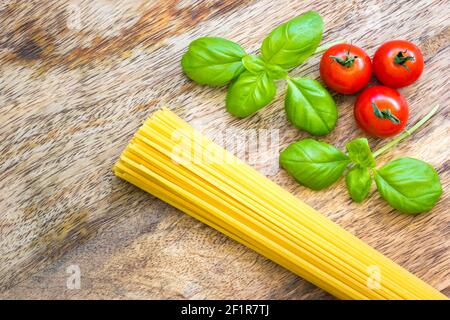 Getrocknete Spaghetti mit rohen Tomaten und frischem Basilikum auf einem Holzbrett Stockfoto