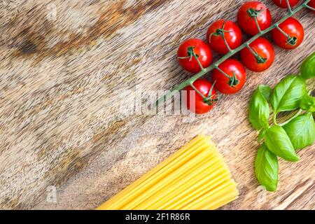 Frisches Basilikum neben reifen Tomaten und getrockneten Spaghetti auf einem Holzbrett Stockfoto