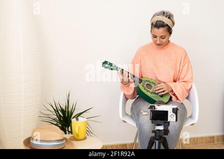 Eine Spanierin nimmt sich selbst auf, während sie auf einem Grün spielt Ukulele in einem modernen Studio Stockfoto