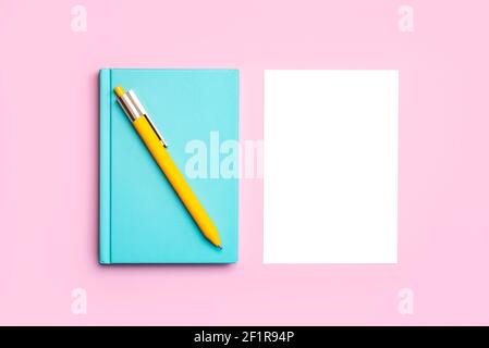 Schreibtisch mit blauem Notizblock, gelbem Stift und weißem Papier mit Kopieren Sie den Hintergrund des Raums auf einen rosa Hintergrund Stockfoto
