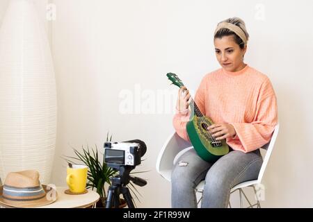 Eine Spanierin nimmt sich selbst auf, während sie auf einem Grün spielt Ukulele in einem modernen Studio Stockfoto