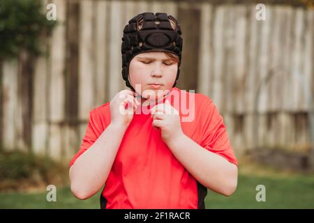 Junge, der Rugby-Schutzkopfausrüstung im Hinterhof aufsetzt Stockfoto