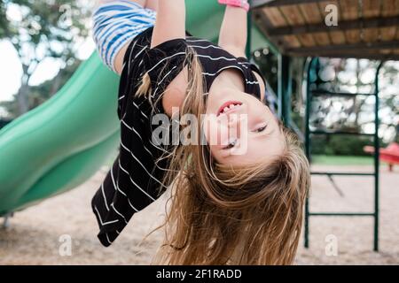 Junge glückliche Mädchen hängen kopfüber auf einem öffentlichen Spielplatz Stockfoto