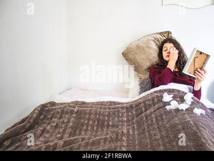 Junge Frau liegt weinend mit Foto und Taschentücher im Bett Stockfoto