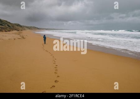 Junge Frau, die allein am Strand gegen raue Meereswellen des südlichen Ozeans, Victoria Australien, läuft. Stockfoto