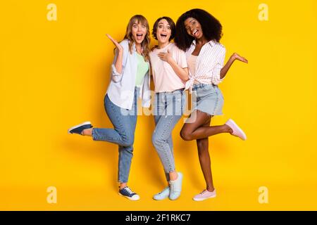 Foto in voller Größe von schönen optimistischen drei Damen tanzen tragen Weißes Hemd Jeans isoliert auf gelbem Hintergrund Stockfoto