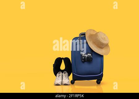 Blaues Handgepäck mit Rädern und wichtige Reiseartikel vor gelbem Hintergrund. Stockfoto