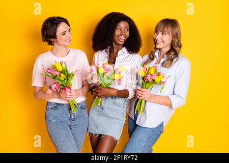 Foto von schönen optimistisch drei Damen halten Blumen tragen weiß shirt isoliert auf hellgelben Hintergrund Stockfoto