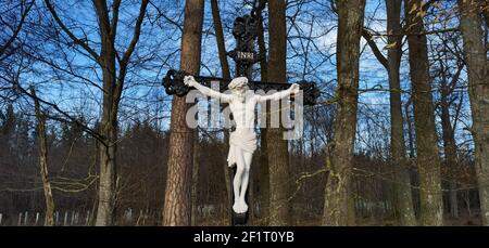 Kreuz und Jesus Christus Statue auf Wald Hintergrund. Religiöses Symbol. Katholizismus und Christentum.Denkmäler und Statuen in Europa. Friedhof und Stockfoto