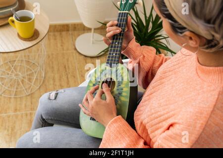 Eine nicht erkennbare Frau, die auf einer grünen Ukulele in einem spielt Modernes Studio Stockfoto