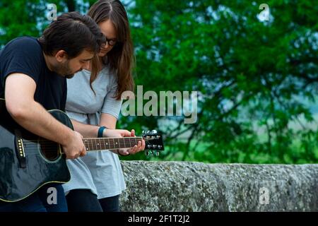 Der ältere Bruder lehrt seine jüngere Schwester, Gitarre in der Natur zu spielen. Schöne Momente zusammen verbracht Stockfoto