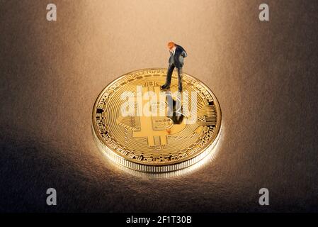 Geschäftsmann Miniatur Figur stehend auf einem gold Bitcoin nach unten schauen, Nachdenken über die Risiken und Erträge von Investitionen in die cryptocurrency Stockfoto