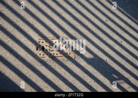 Eiserne Zugangsabdeckung auf einer Straße. Metallabdeckung auf einer Straße. Zaunschatten auf Asphalt. Abstrakter Hintergrund. Stockfoto