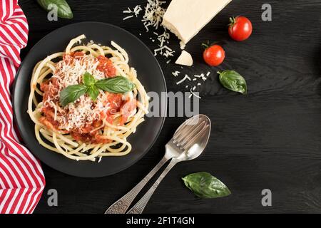 Italienische Pasta mit Tomatensauce und Parmesan auf dem schwarzen Teller auf dem dunklen Holzhintergrund. Draufsicht. Speicherplatz kopieren. Stockfoto