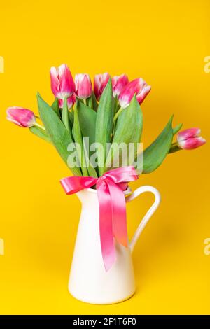 Nahaufnahme eines weißen Porzellantopfes aus blühendem Rosa Tulpen vor einem durchgehenden gelben Hintergrund Stockfoto