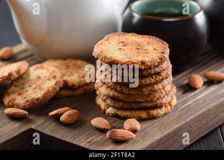 Stapel von Mandelgebäck, rohen Mandeln und schwarzem Tee auf Eichenbrett Nahaufnahme Stockfoto